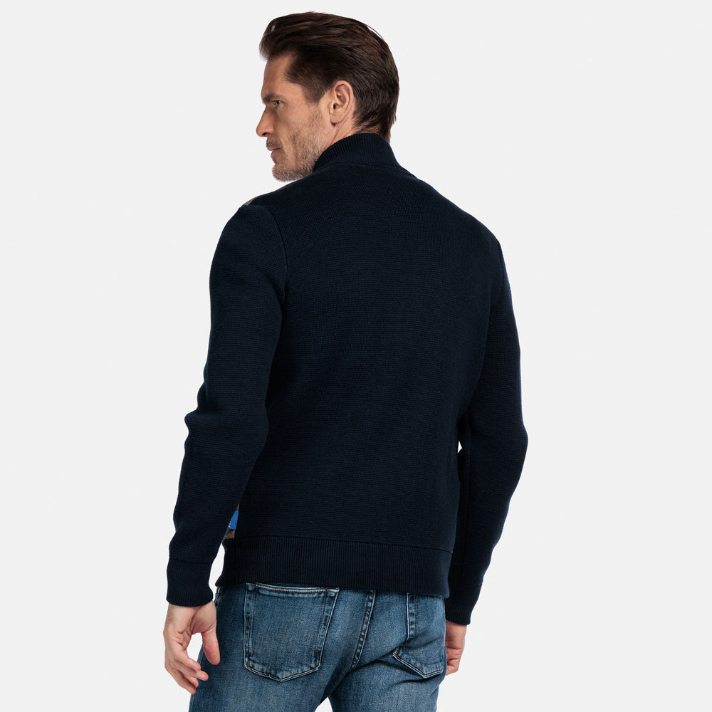 Man wearing a dark blue sweater and jeans on a light gray background