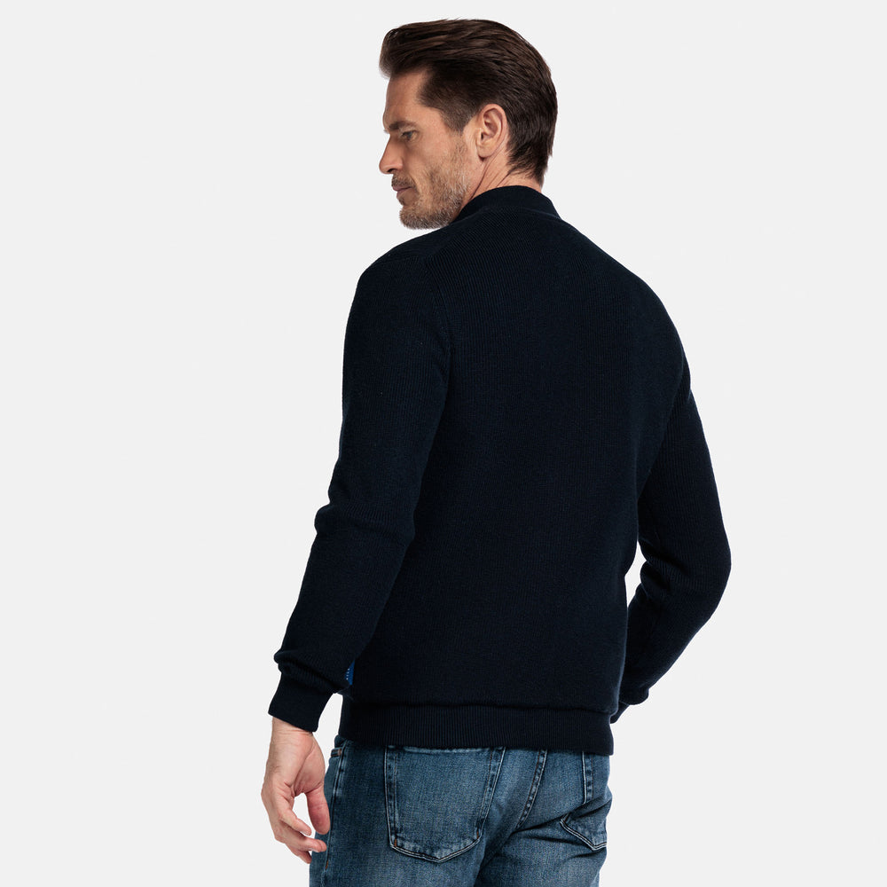 Man wearing a Navy cardigan jacket and blue jeans on a light gray background