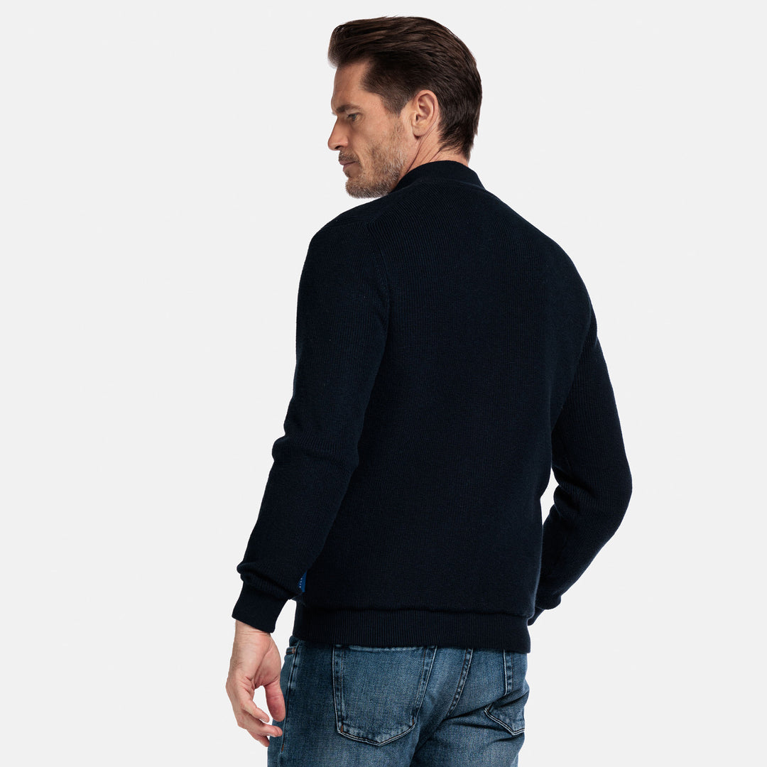 Man wearing a Navy cardigan jacket and blue jeans on a light gray background