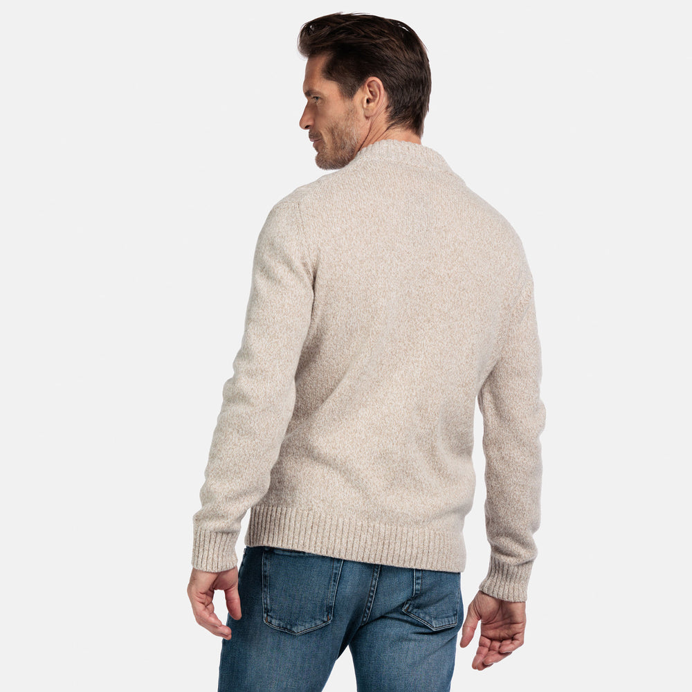 Man wearing a beige sweater and blue jeans on a white background