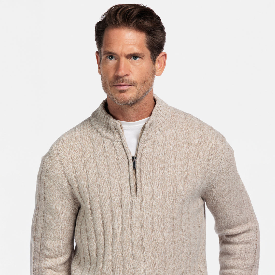 Man wearing a beige cable knit sweater with a white background