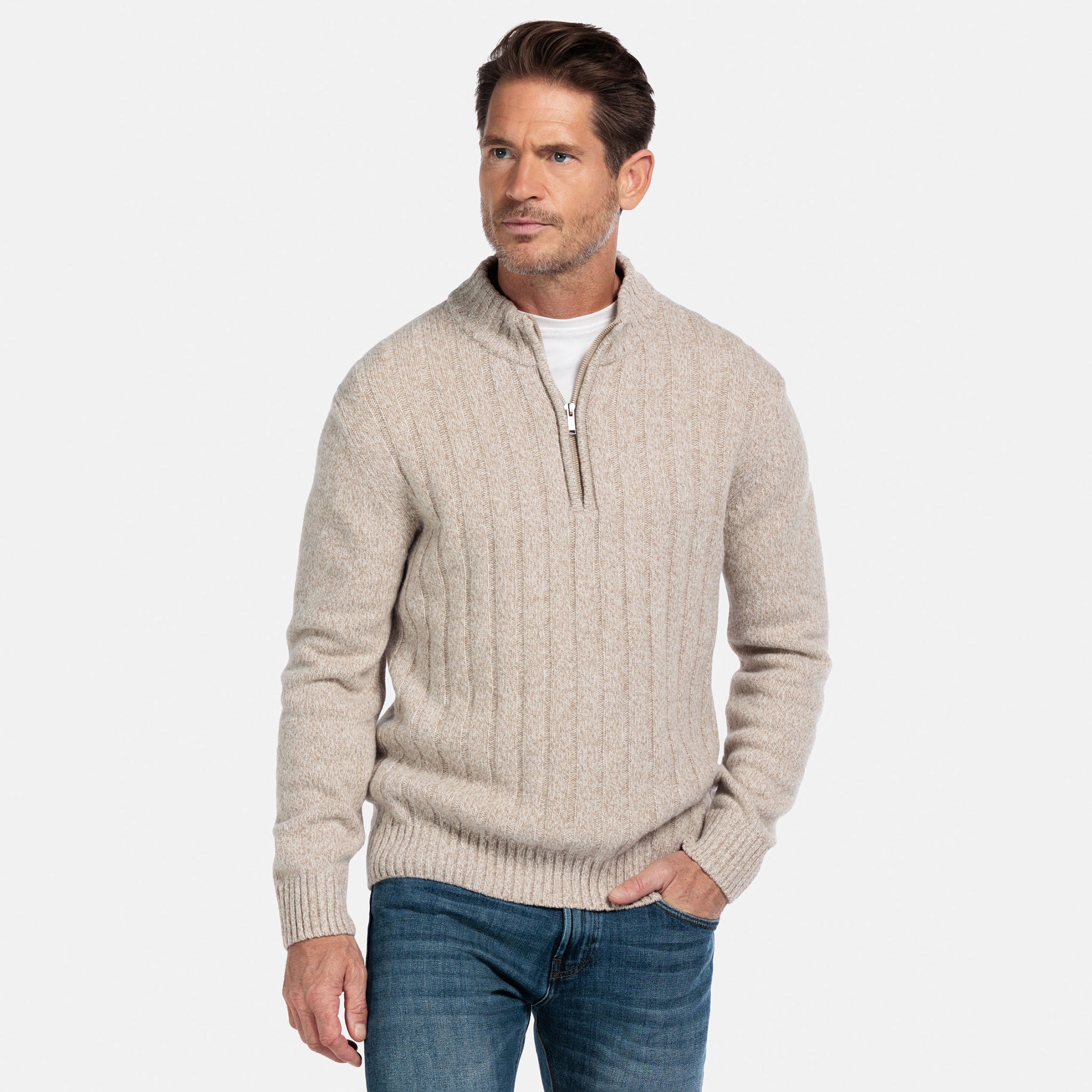 Man wearing a beige half-zip sweater and blue jeans on a white background