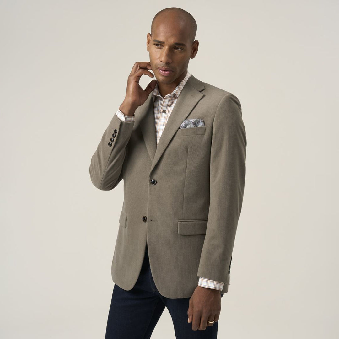 Man wearing a beige blazer with a white shirt and dark pants on a plain background