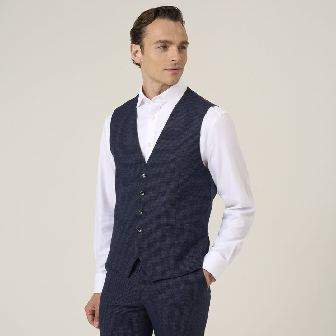 Man wearing a navy vest over a white shirt against a plain background