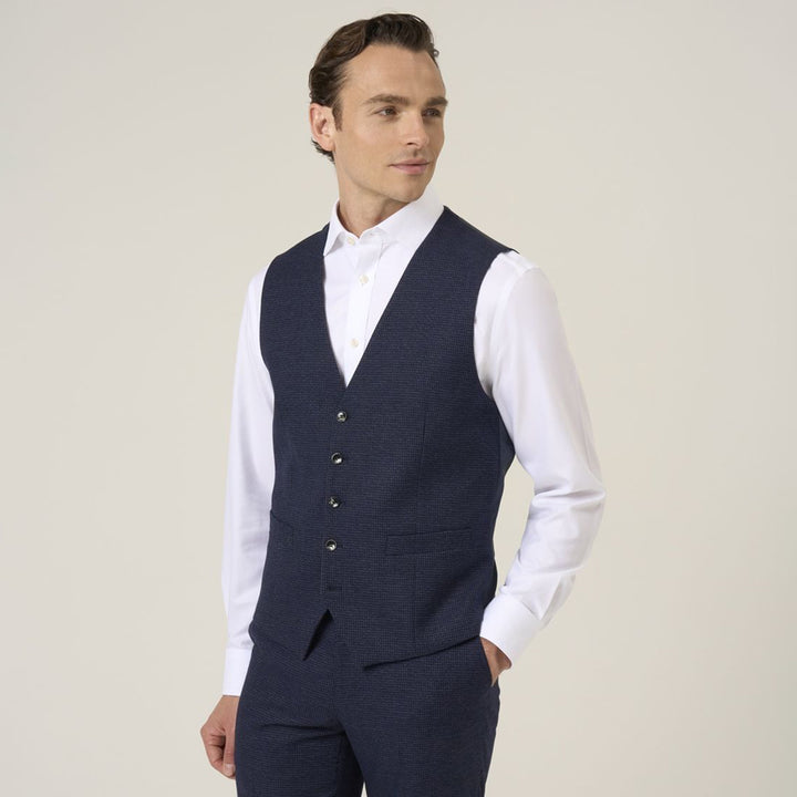 Man wearing a navy vest over a white shirt against a plain background