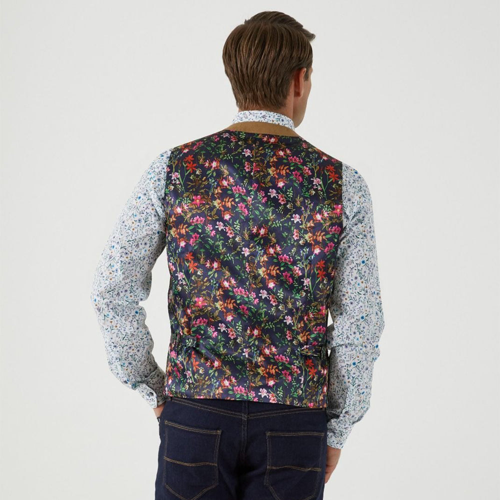 Person wearing a floral vest over a patterned shirt on a plain background