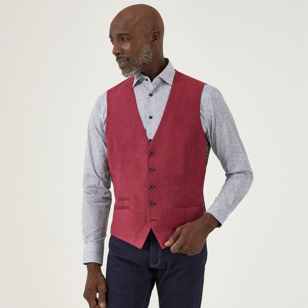 Man wearing a red vest over a patterned shirt on a plain background