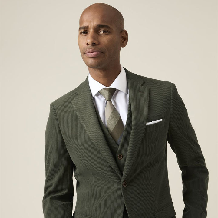 Man wearing a green suit with a white shirt and patterned tie on a beige background