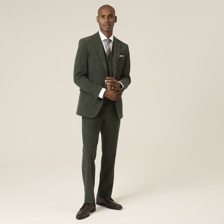 Man wearing a green suit with a white shirt and brown shoes on a beige background