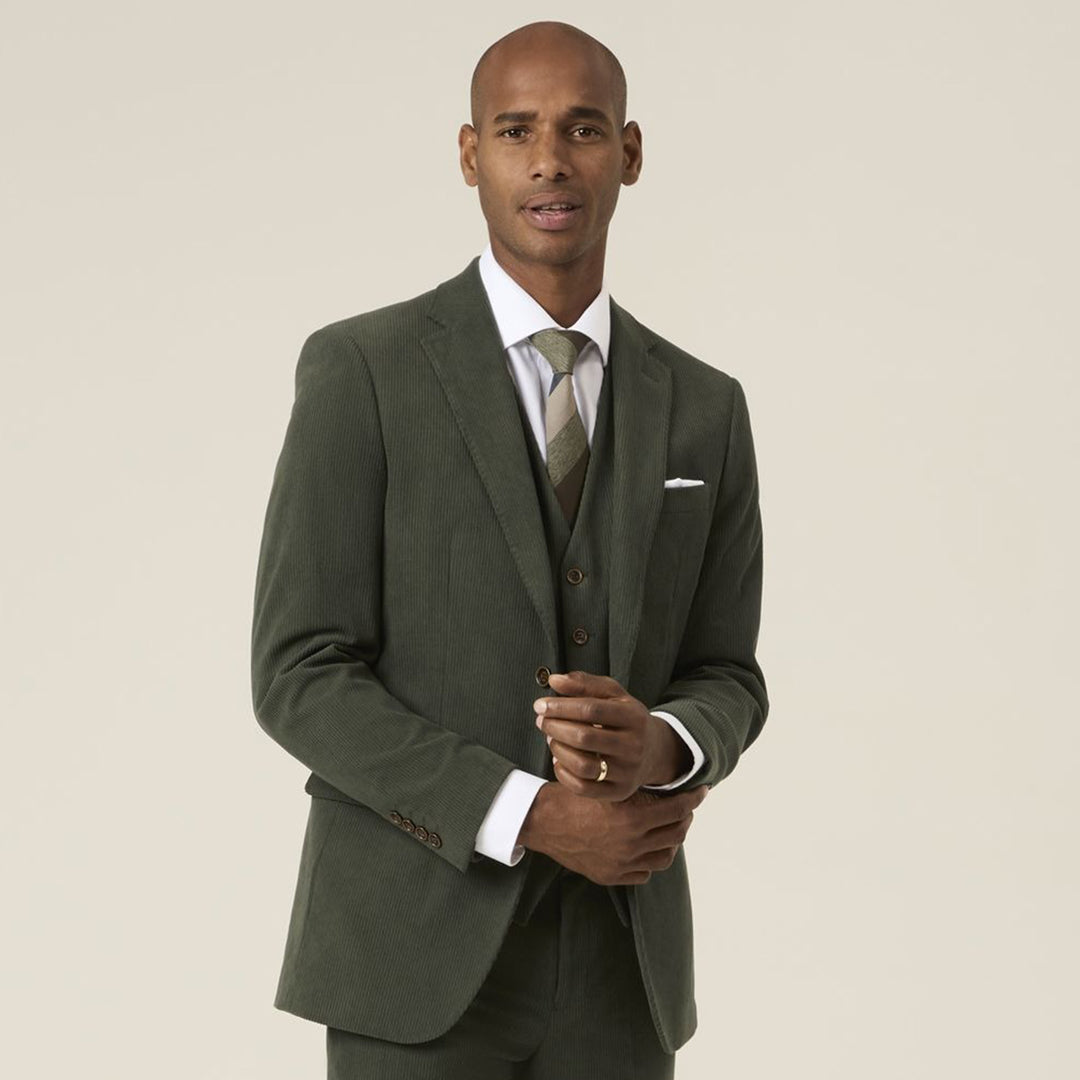 Man wearing a green suit with a white shirt and patterned tie on a beige background