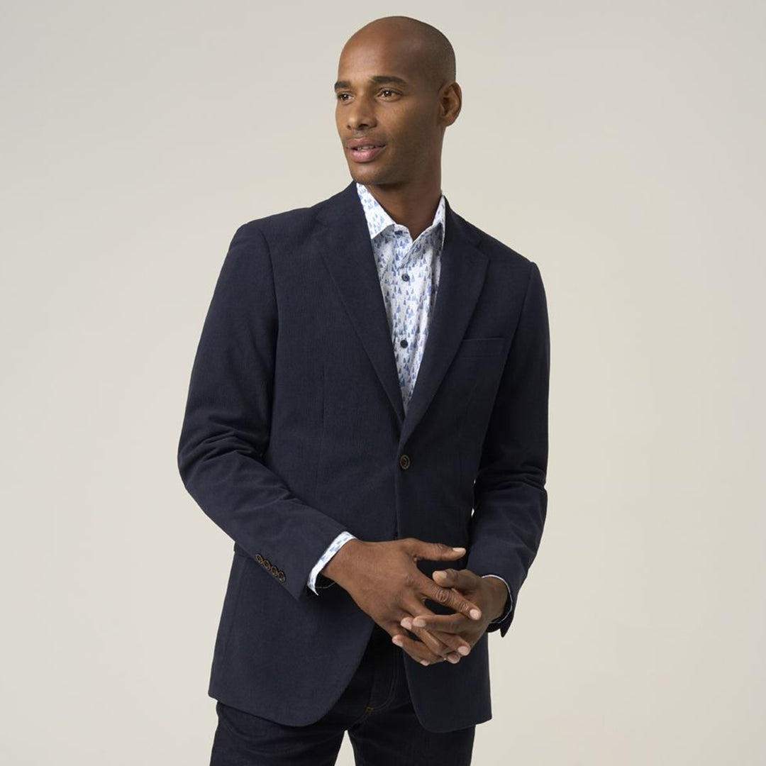 Man wearing a navy blazer over a patterned shirt on a plain background