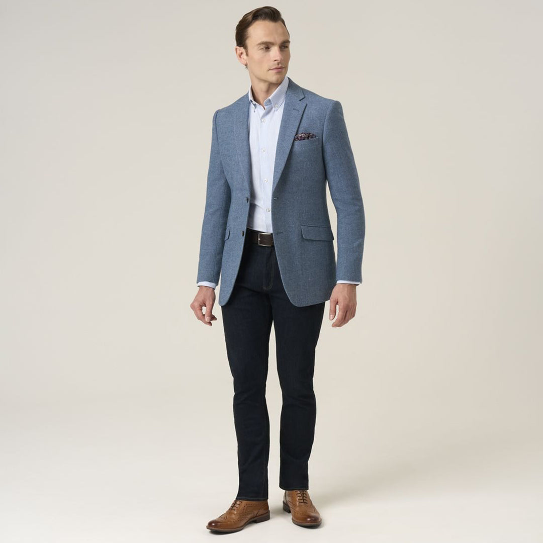 Man wearing a blue blazer, white shirt, black pants, and brown shoes on a plain background