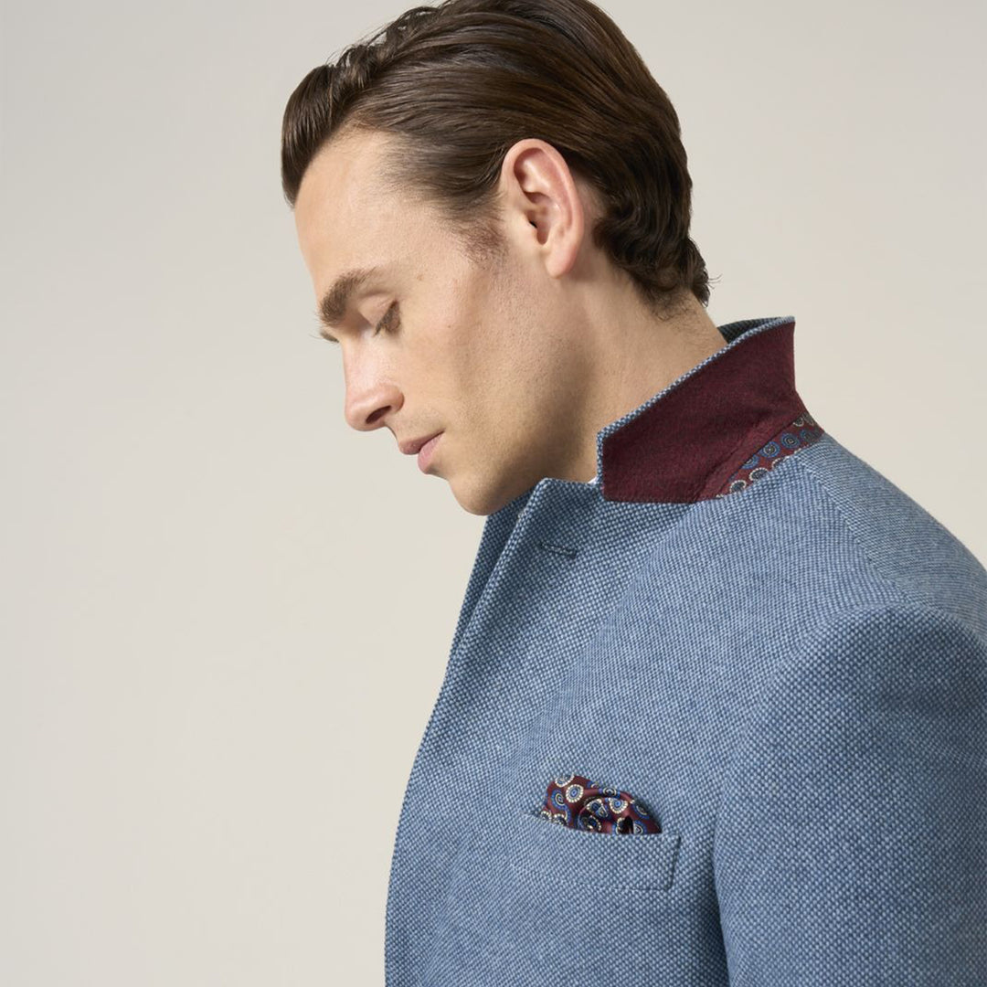 Man wearing a blue suit with a patterned pocket square on a neutral background