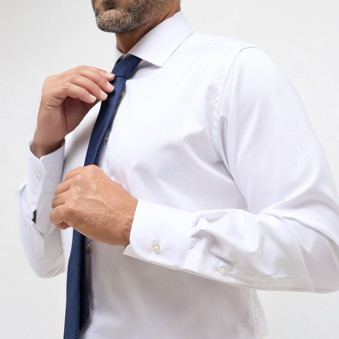 Man adjusting a blue tie on a white shirt against a plain background