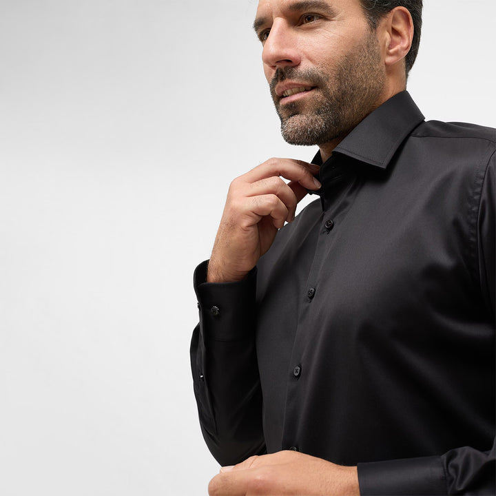 Man adjusting his black dress shirt against a light gray background