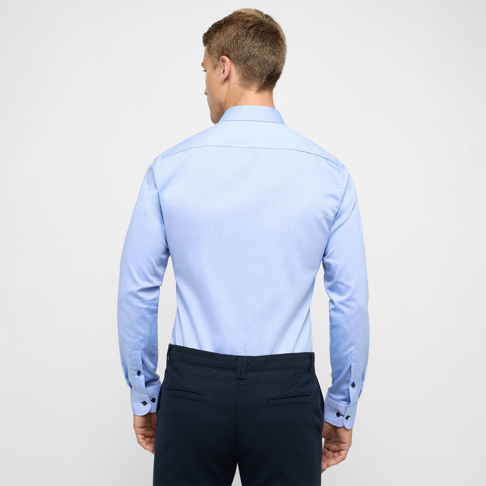Man wearing a light blue dress shirt and dark pants on a white background