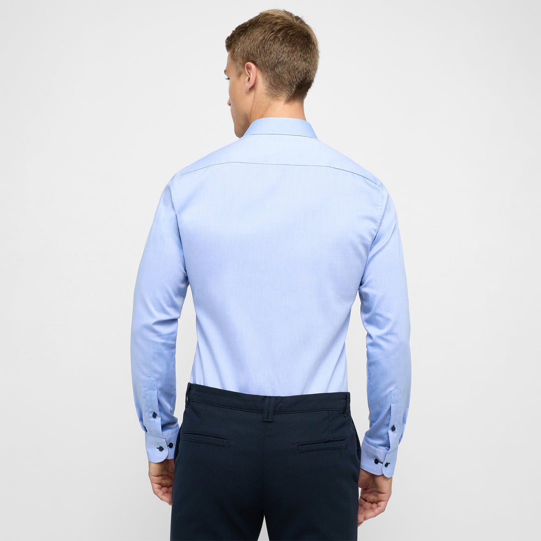 Man wearing a light blue dress shirt and dark pants on a white background