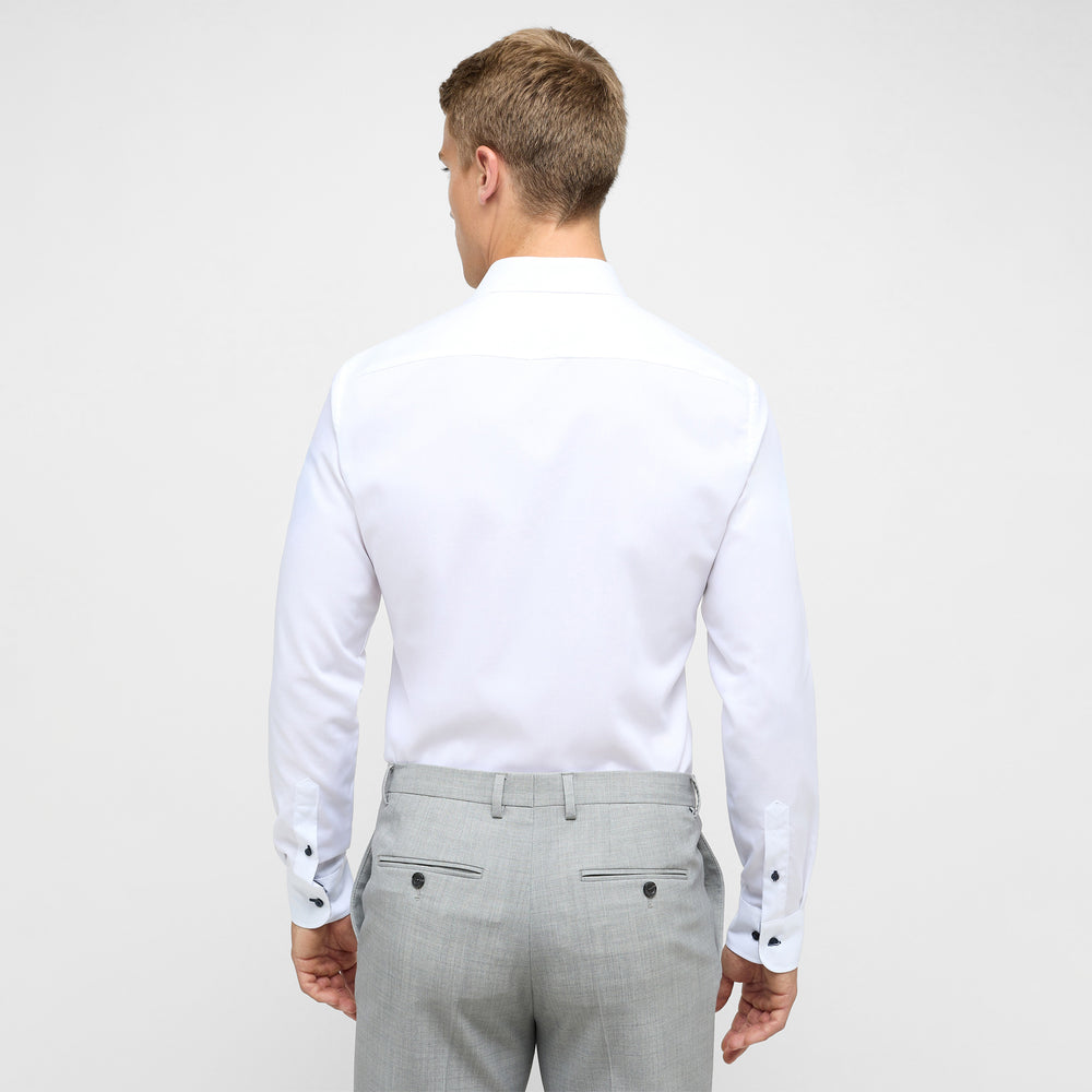 Man wearing a white dress shirt and gray pants on a plain background