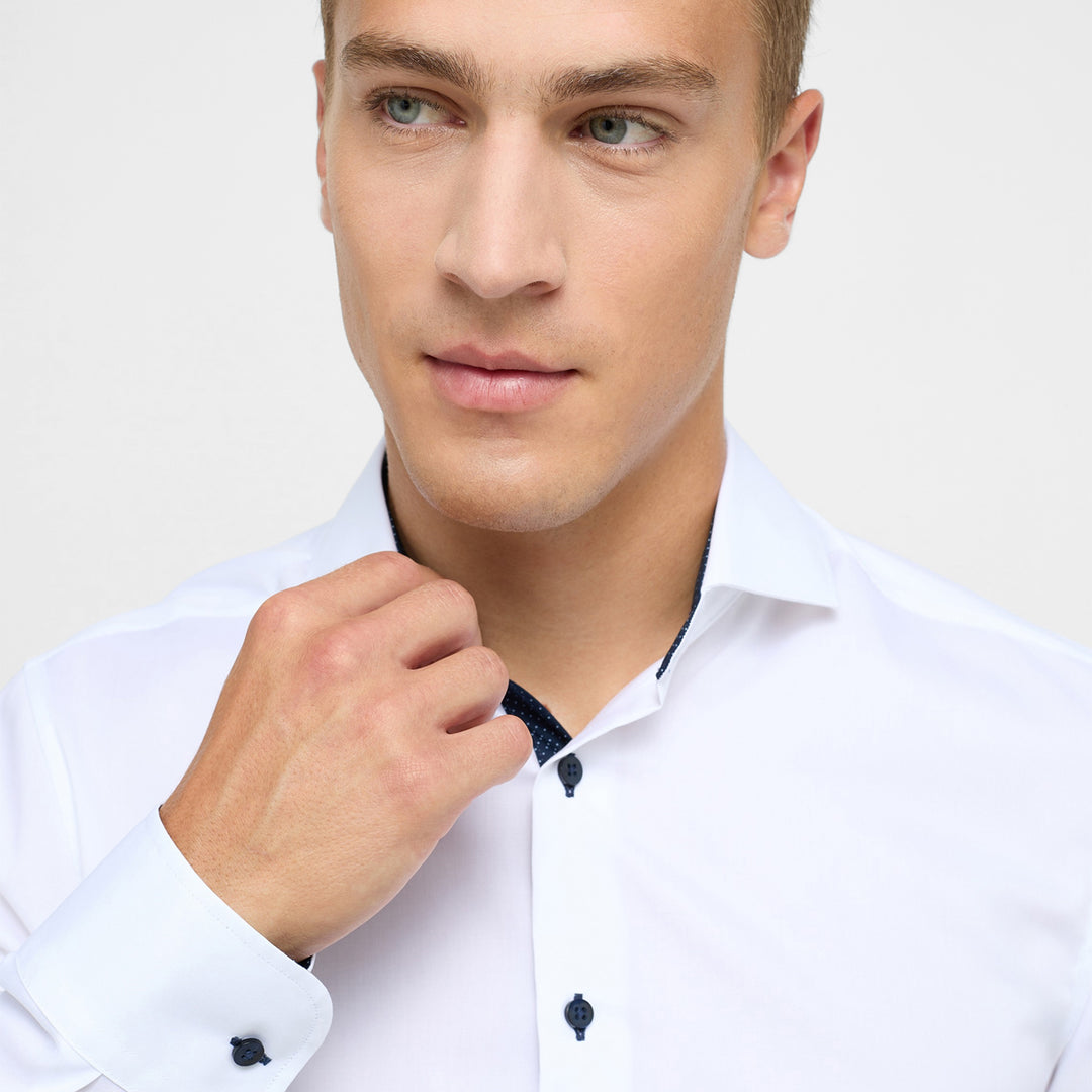 Man adjusting his white shirt collar against a plain background