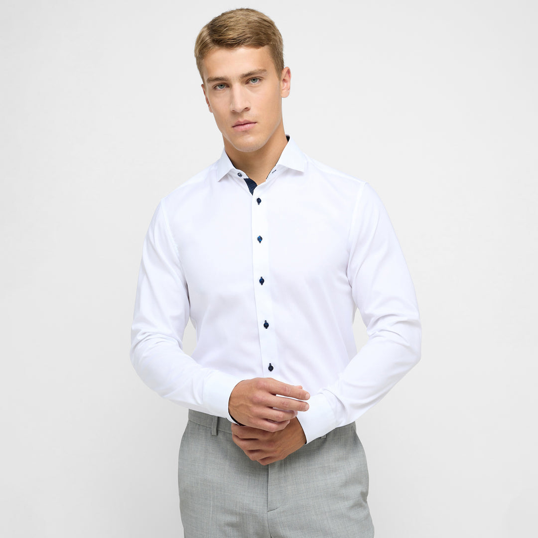 Man wearing a white dress shirt with black buttons and gray pants on a light gray background