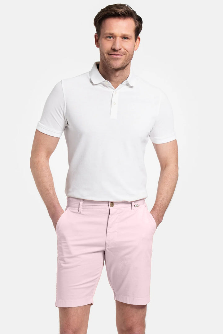 Man wearing a white polo shirt and pink shorts on a white background