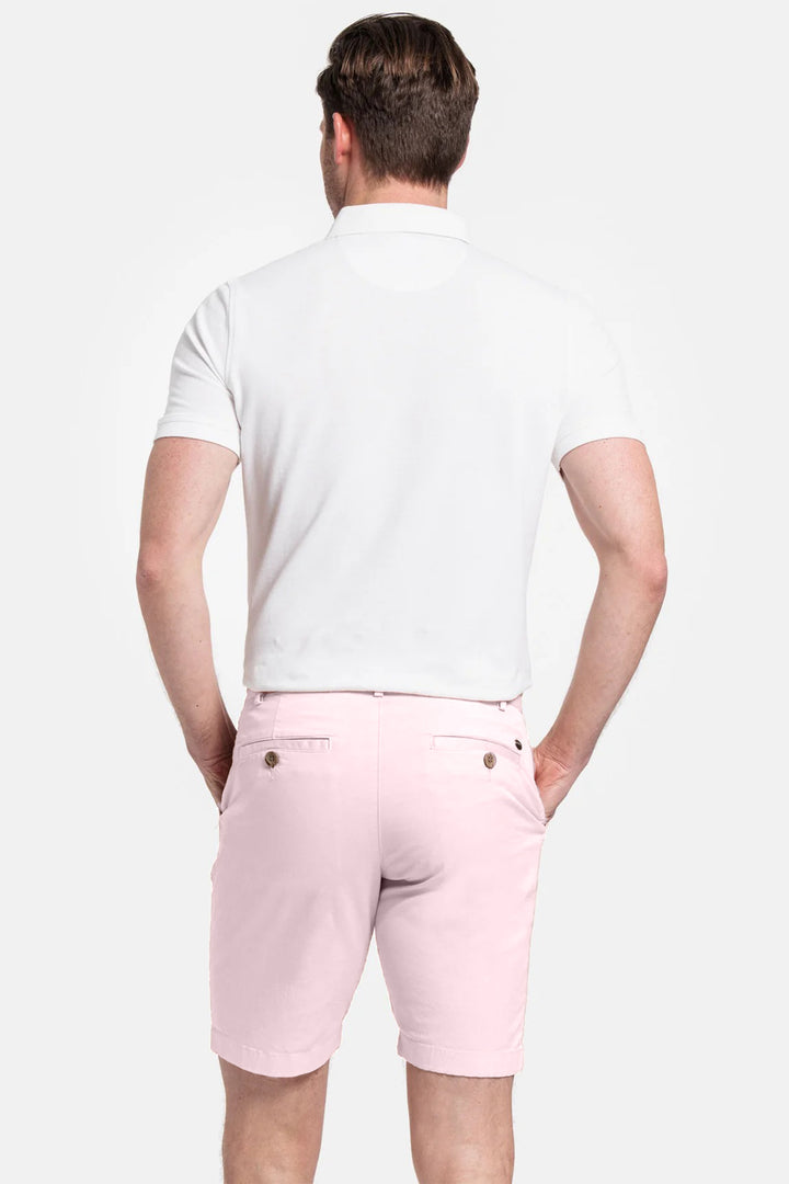 Person wearing a white polo shirt and pink shorts on a light gray background