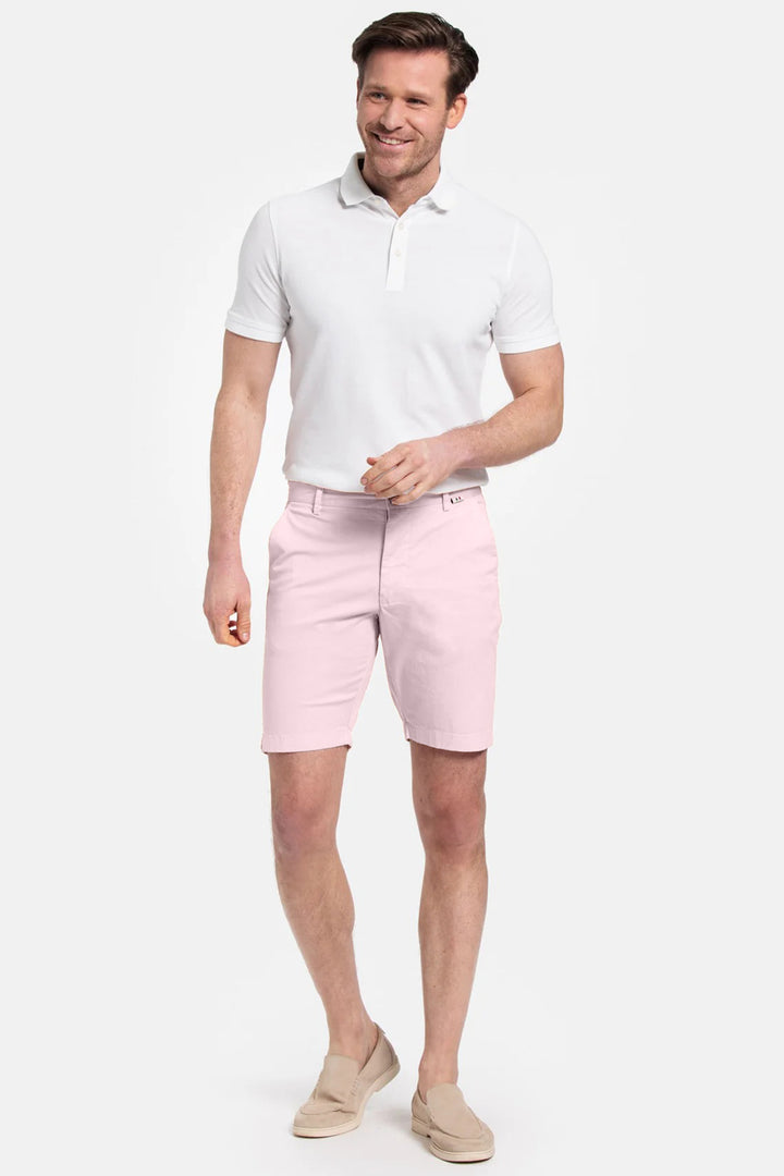 Man wearing a white polo shirt and pink shorts on a white background