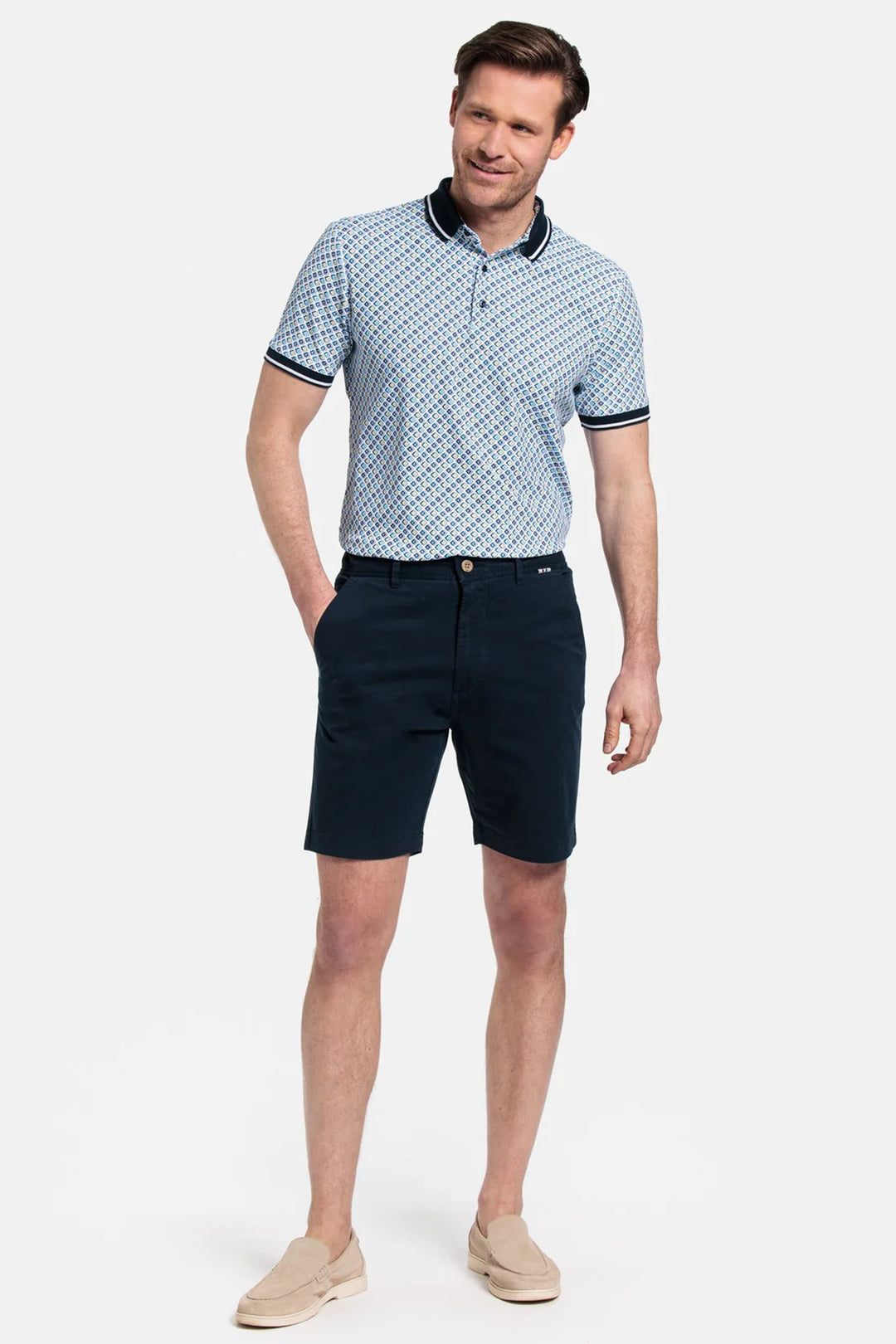 Man wearing a patterned polo shirt and navy shorts on a white background
