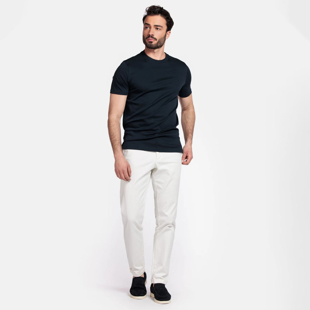 Man wearing a navy t-shirt and white pants on a white background
