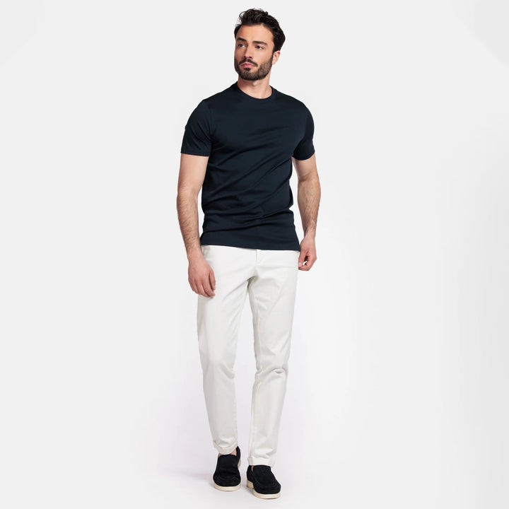 Man wearing a navy t-shirt and white pants on a white background