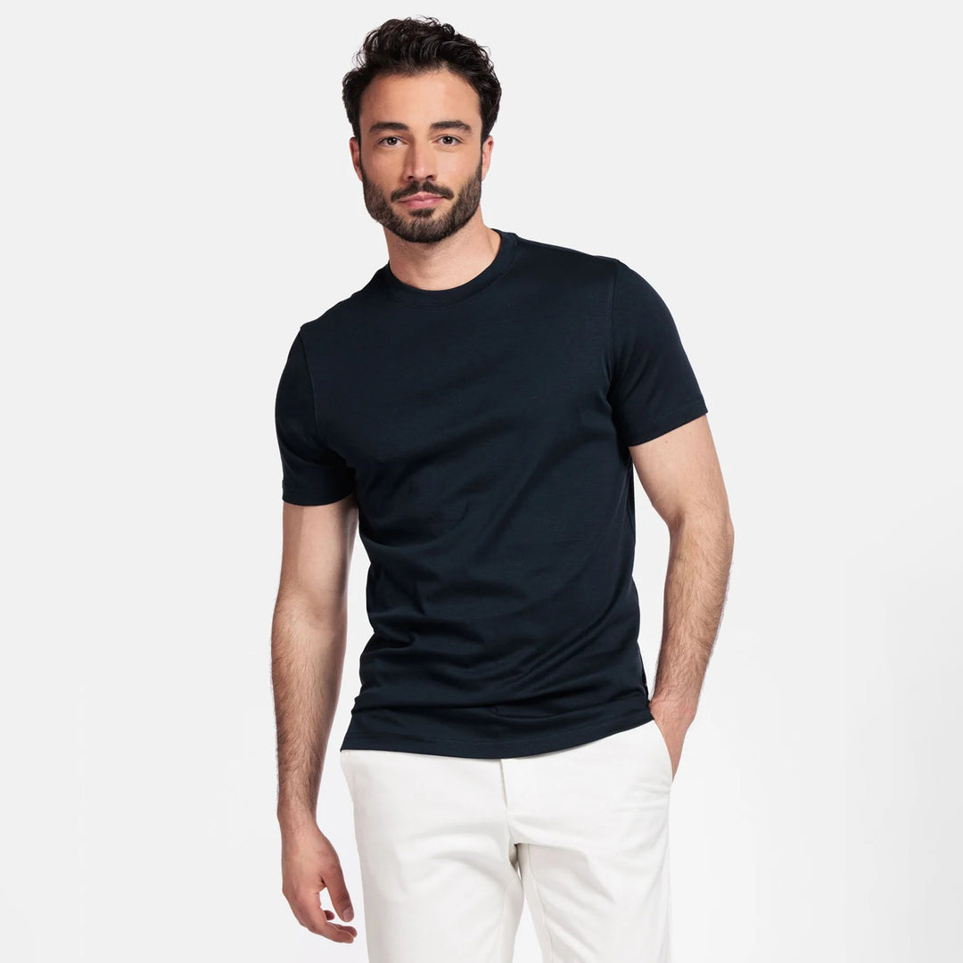 Man wearing a navy t-shirt and white pants on a plain background