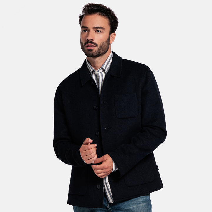 Man wearing a black jacket over a white shirt on a plain background