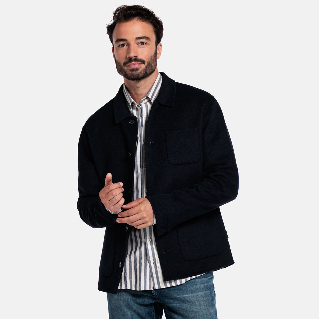 Man wearing a black jacket over a striped shirt on a white background