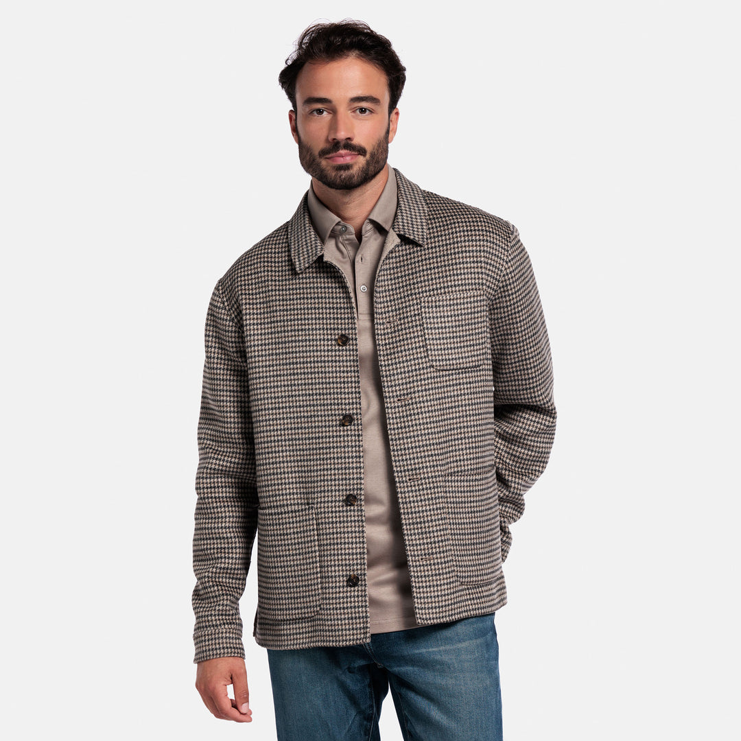 Man wearing a checkered shirt over a button-up shirt with a plain background