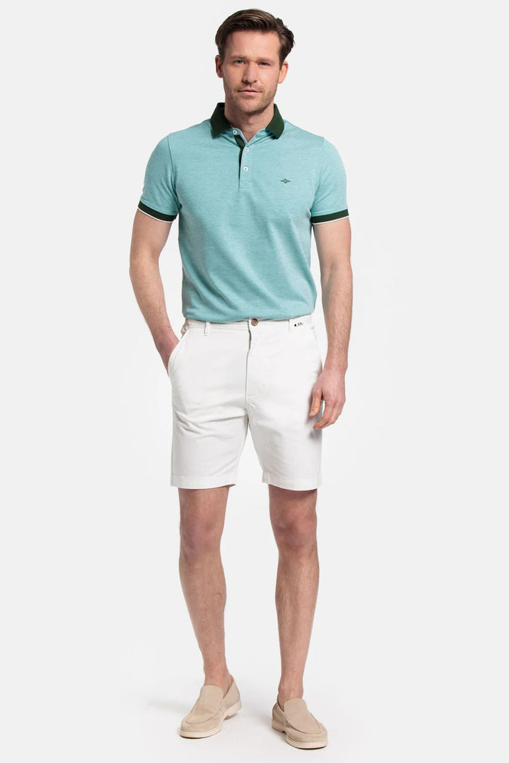 Man wearing a light blue polo shirt with green trim and white shorts on a white background