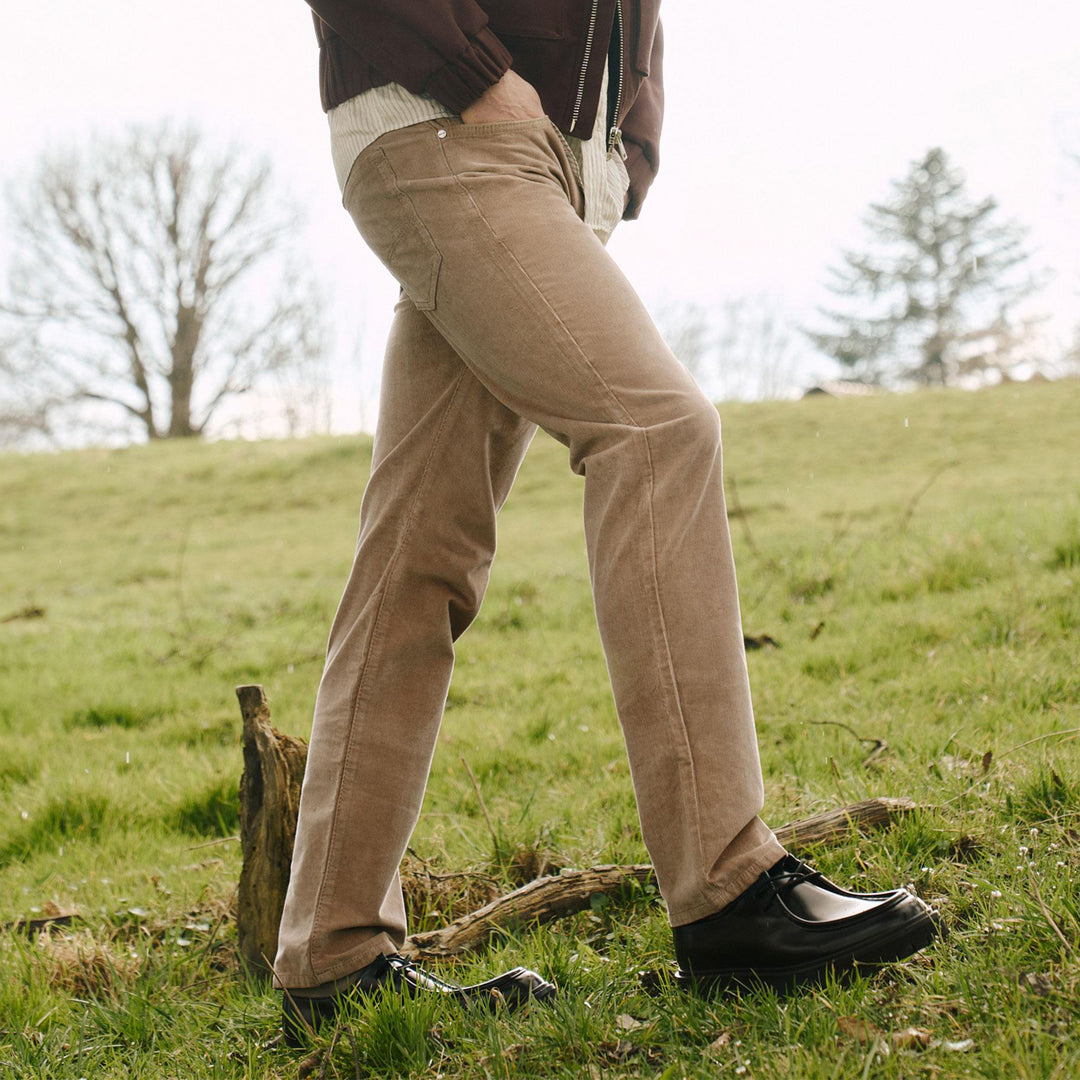 Person wearing beige pants and black shoes standing on a grassy field.
