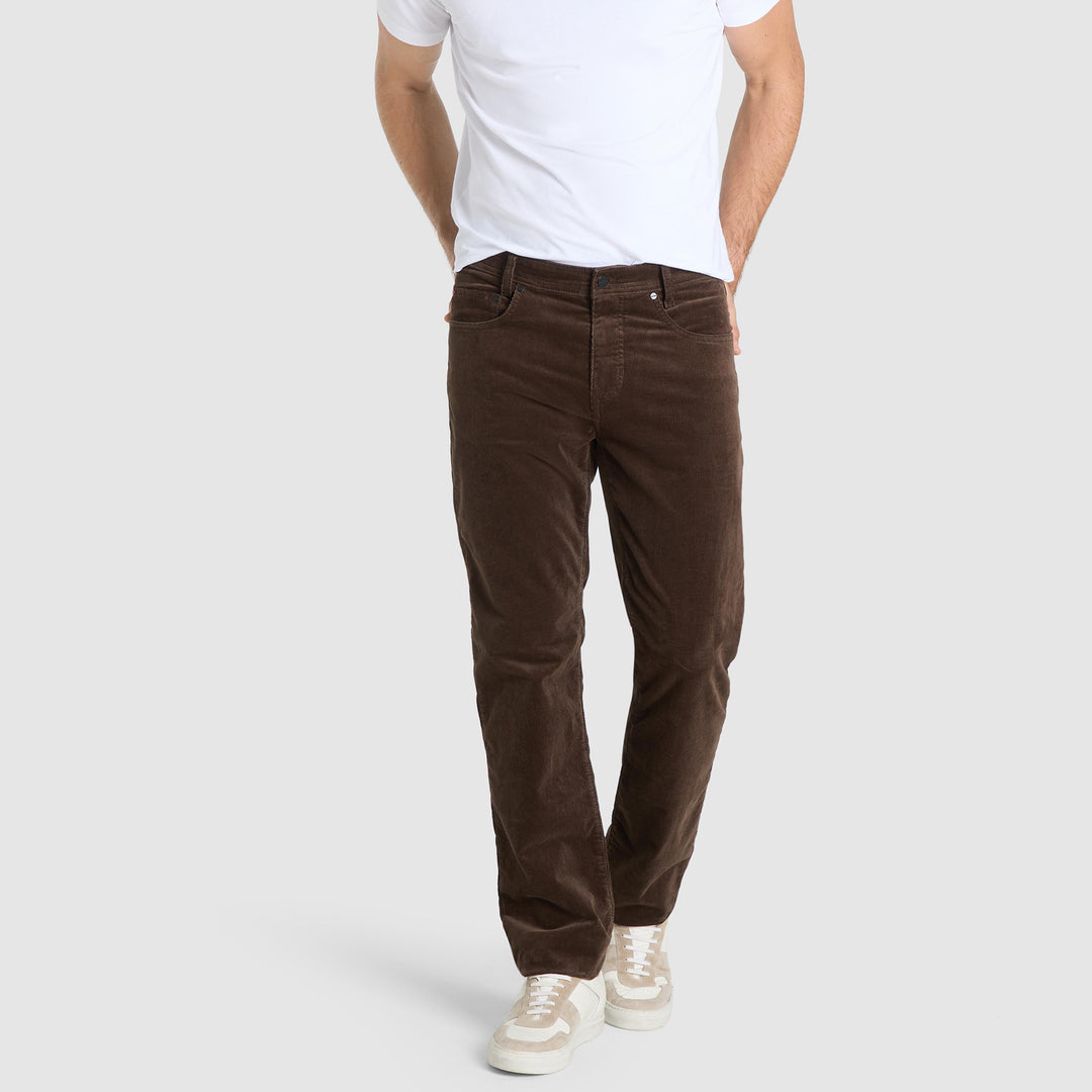 Person wearing brown corduroy pants and a white t-shirt on a light gray background