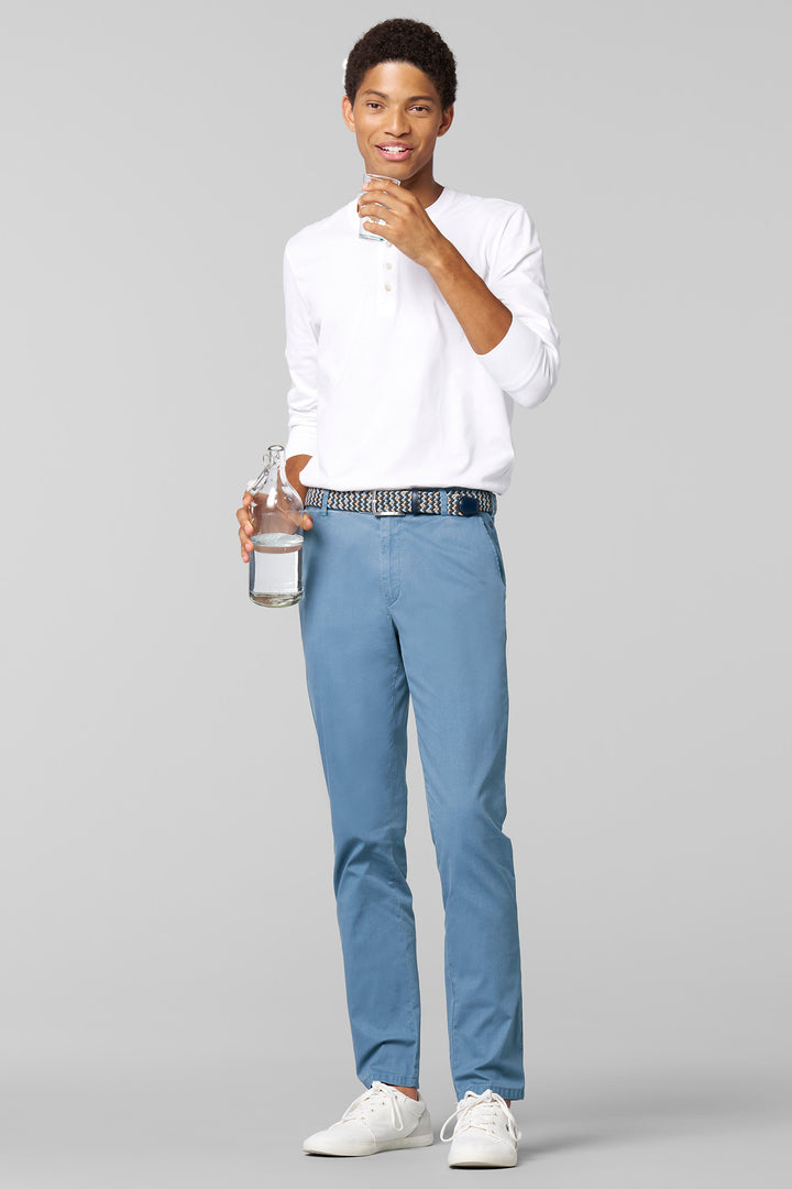 Man wearing a white shirt, blue pants, and white sneakers holding a water bottle on a gray background