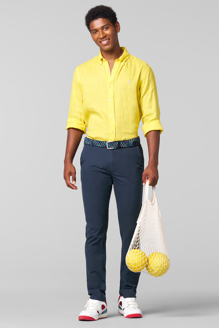 Man wearing a yellow shirt and navy pants holding a white bag with yellow balls on a gray background