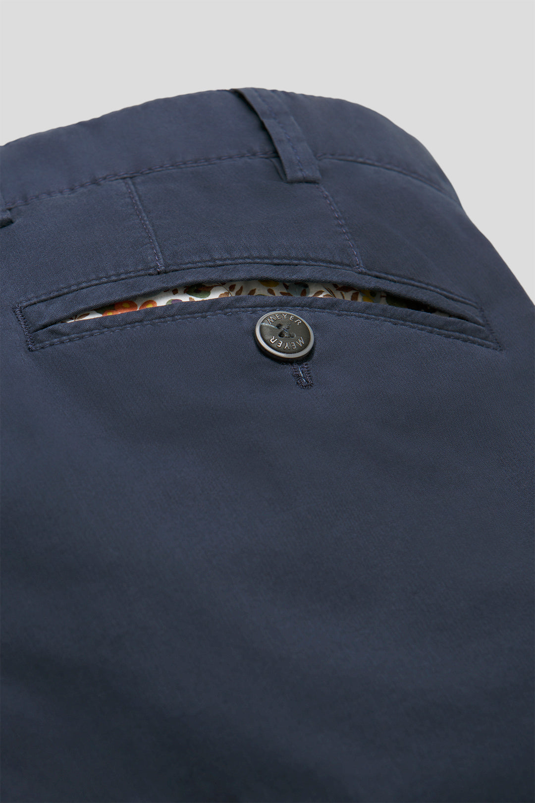 Close-up of a navy blue pants pocket with button and zipper on a light gray background