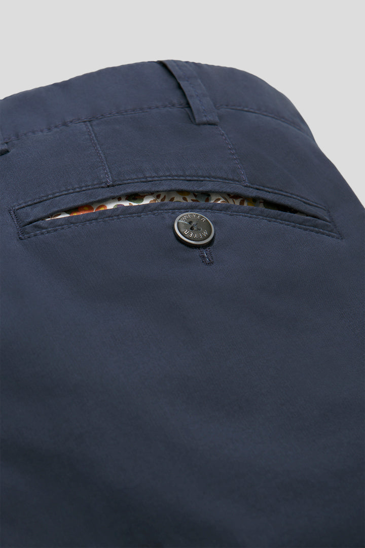 Close-up of a navy blue pants pocket with button and zipper on a light gray background