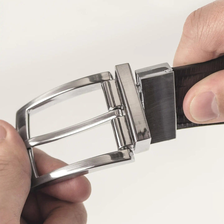 Close-up of a silver belt buckle being adjusted on a black belt against a white background