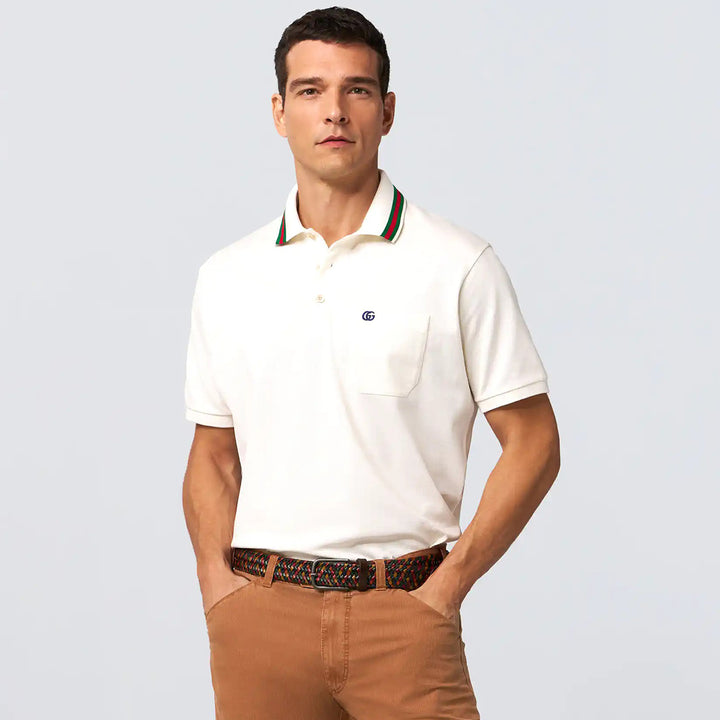 Man wearing a white polo shirt with a brand logo on a light gray background