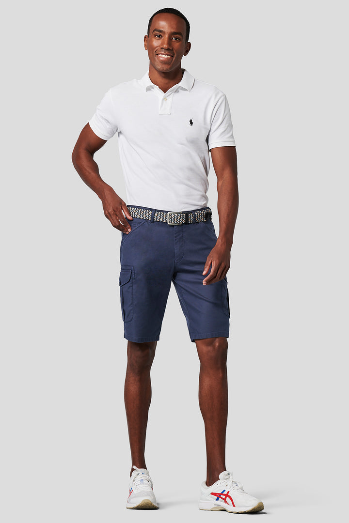 Man wearing a white polo shirt and blue cargo shorts on a light gray background